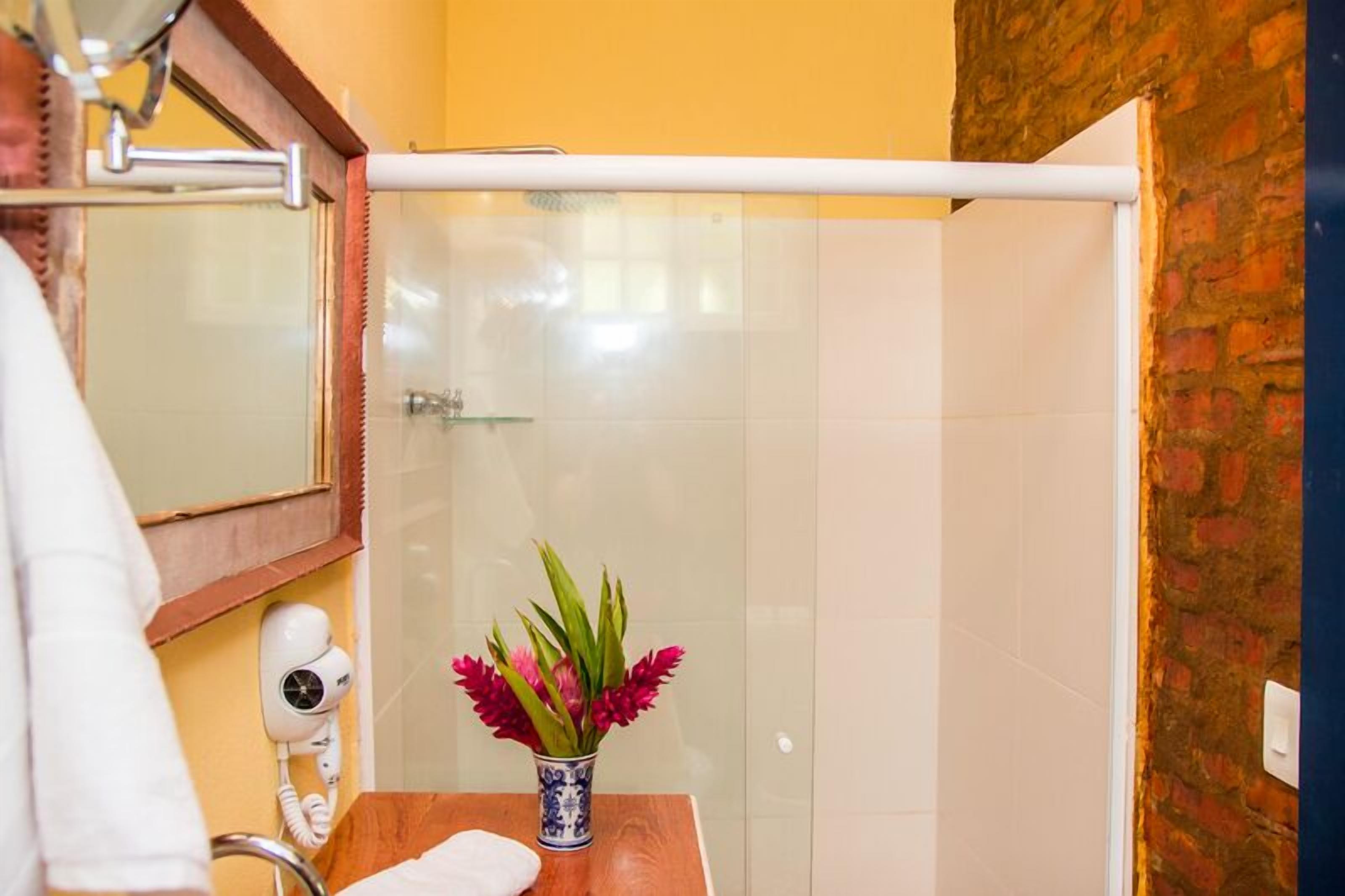 A bathroom with a glass shower enclosure, a white towel on the counter, and a vase with flowers.
