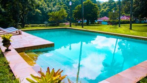 A rectangular swimming pool with a tiled edge, surrounded by grass and potted plants. - Estâncias Duvivier Hotel (Tres Rios)