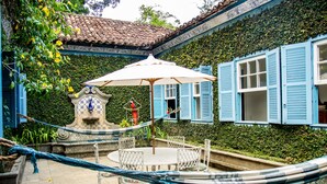 A courtyard with a round table and chairs, a hammock, and a fountain. - Estâncias Duvivier Hotel (Tres Rios)