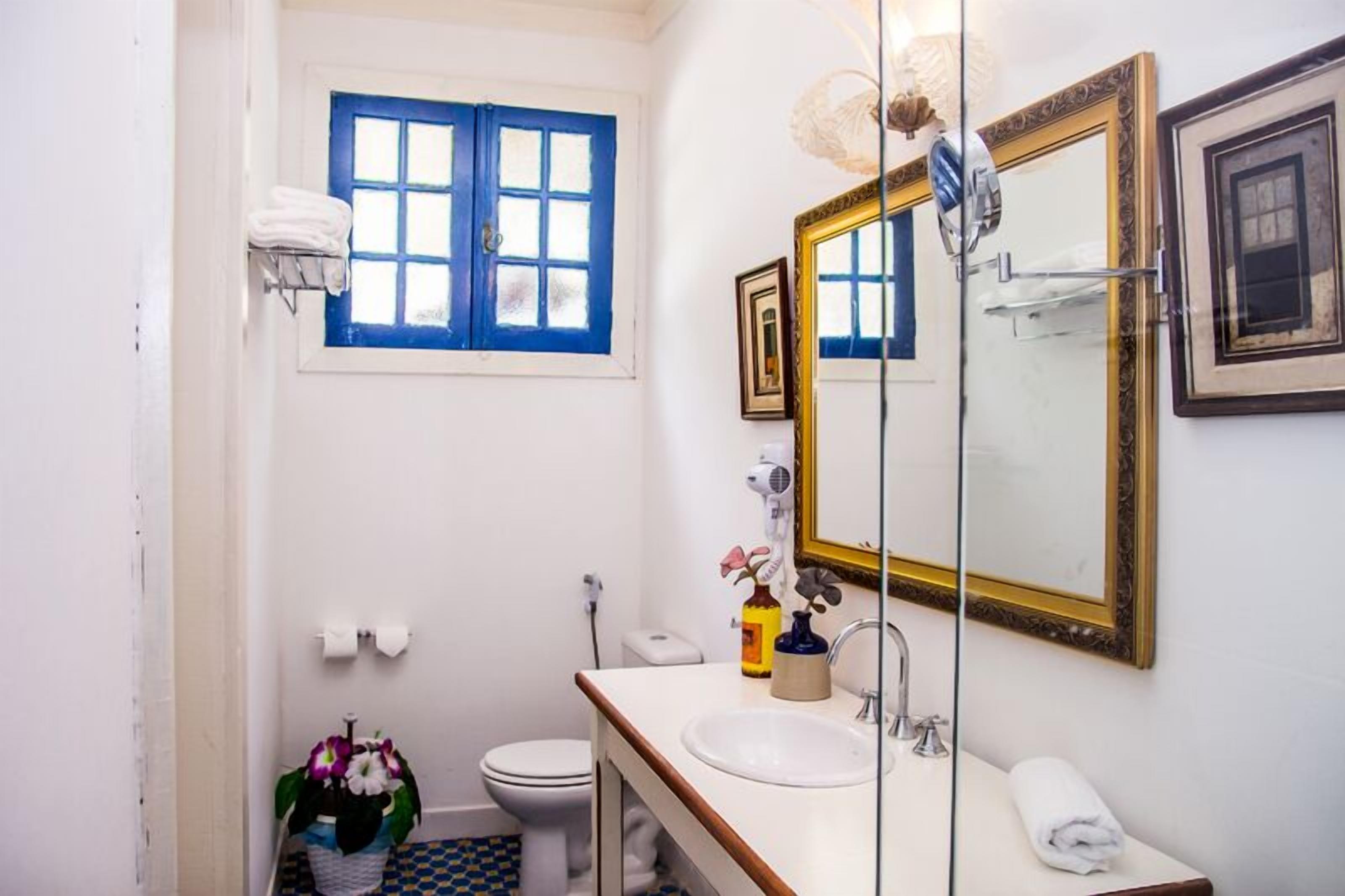 A bathroom with a white sink, a mirror with a gold frame, a toilet, and a window with blue shutters.
