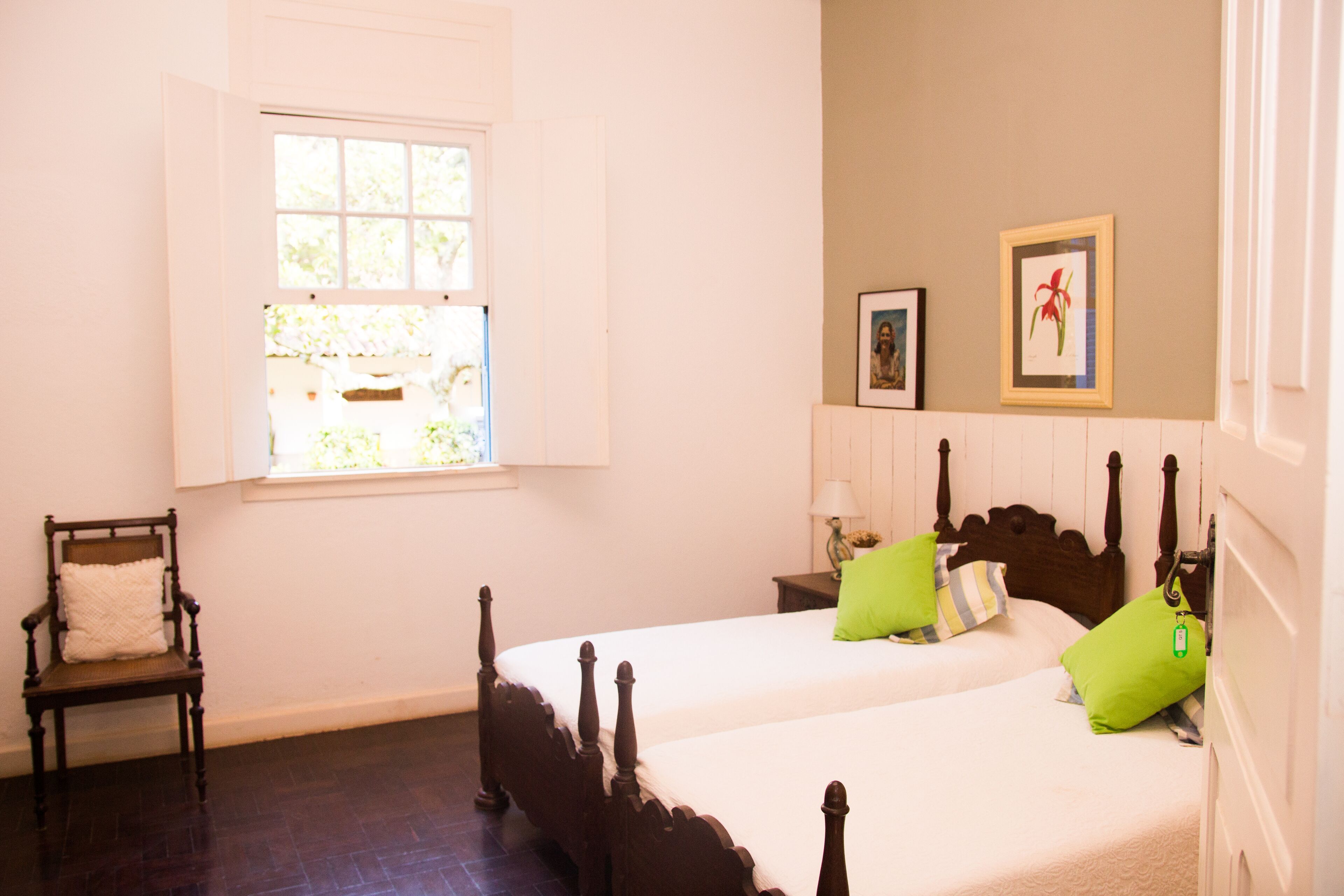 A bedroom with two beds, a chair, a window, and a wall-mounted picture.