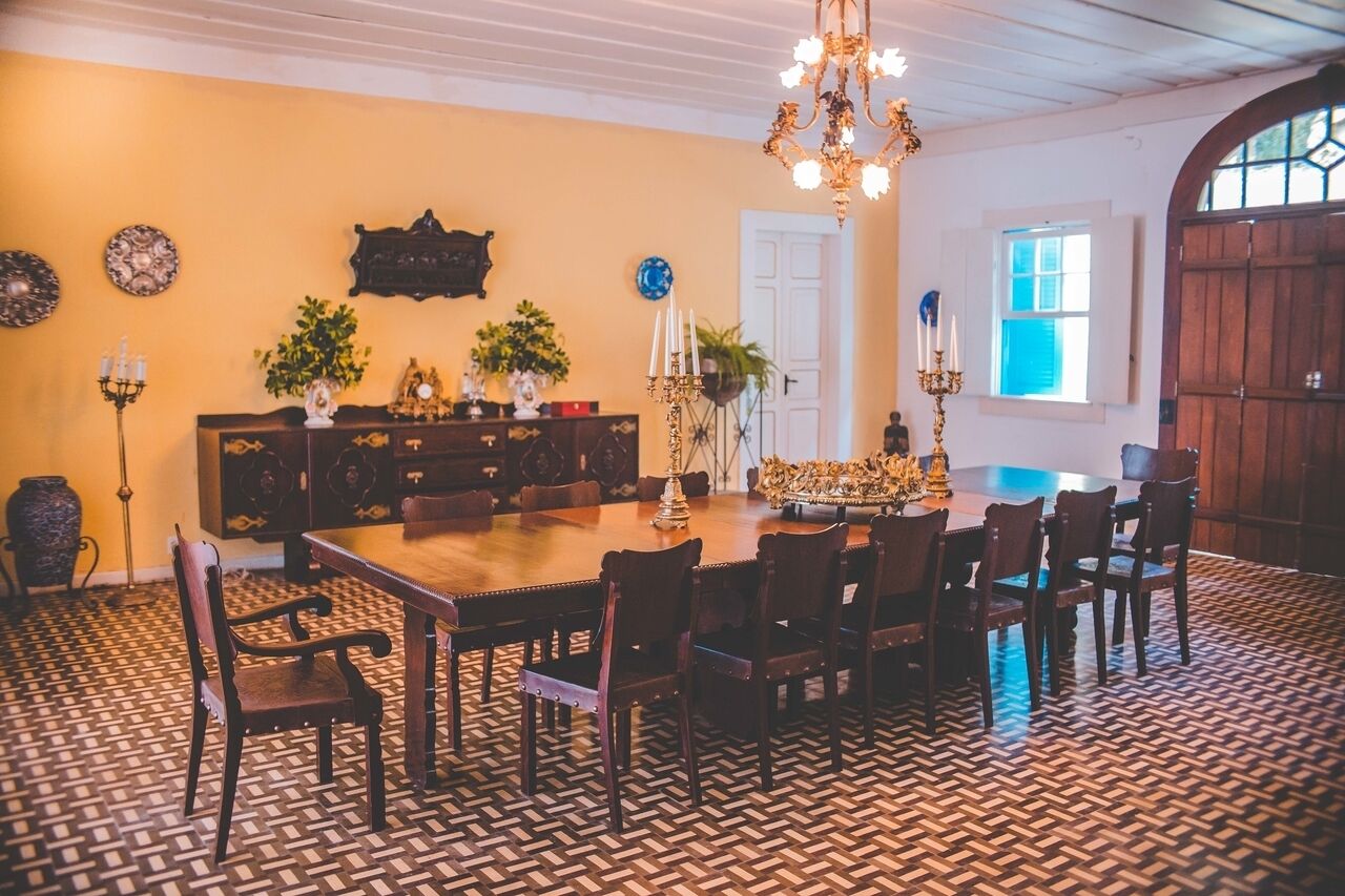 A dining room with a large wooden table, multiple chairs, a chandelier, and a patterned floor.