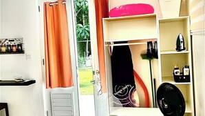 Une chambre dotée d’une porte-fenêtre coulissante donnant sur un jardin, d’une armoire blanche, d’une étagère contenant des articles de toilette et d’une chaise blanche.