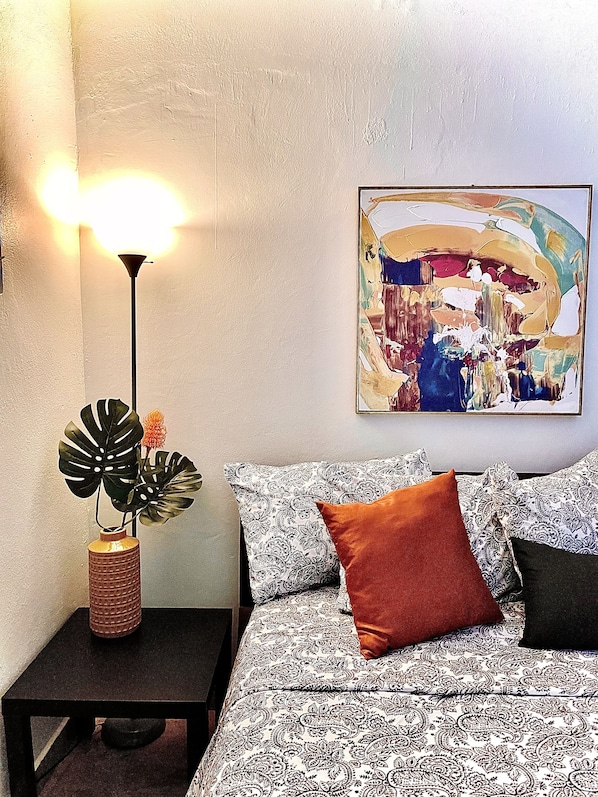 A room with a bed, a nightstand, a floor lamp, and a wall painting.