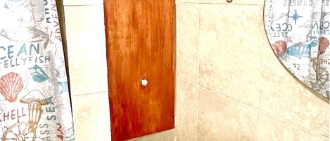 A bathroom with a wooden door, a tiled floor, a white sink, and a shower curtain with a nautical theme.
