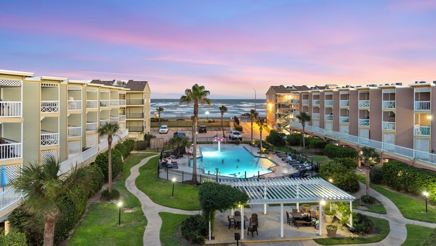 Un hotel con piscina rodeado por un porche cubierto, un camino y vistas al océano.