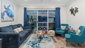 Una sala de estar con sofá, sillones, una mesa de centro y vistas a través de puertas de vidrio.