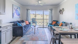 Sala de estar con sofá, mesa de centro y mesa de comedor. Tiene un balcón con vistas a edificios.