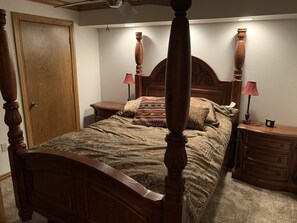 Un lit à baldaquin avec une tête de lit et un pied de lit en bois, flanqué de deux tables de chevet avec des lampes. Une porte en bois est visible sur la gauche.