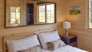 Een houten slaapkamer met een grote spiegel, een bedlamp en een schilderij aan de muur.
