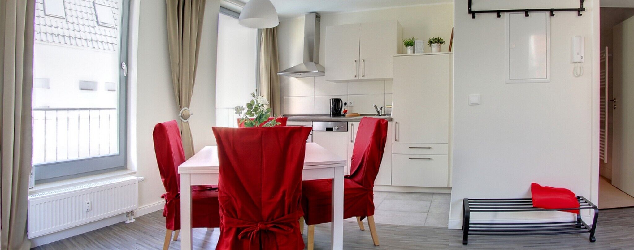 A modern kitchen with white cabinets, a black kettle, and a red chair.