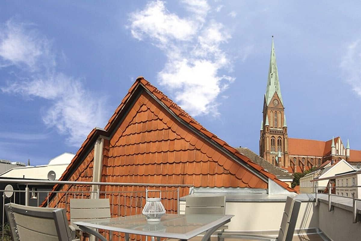 Terraza en la azotea con mesa y sillas, vista a una iglesia con una alta aguja y edificios circundantes.