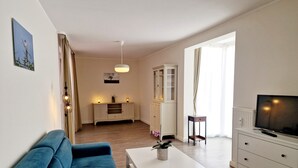 A modern living room with a blue sofa, a white coffee table, and a TV on a cabinet. - Domblick Schwerin (Schwerin)