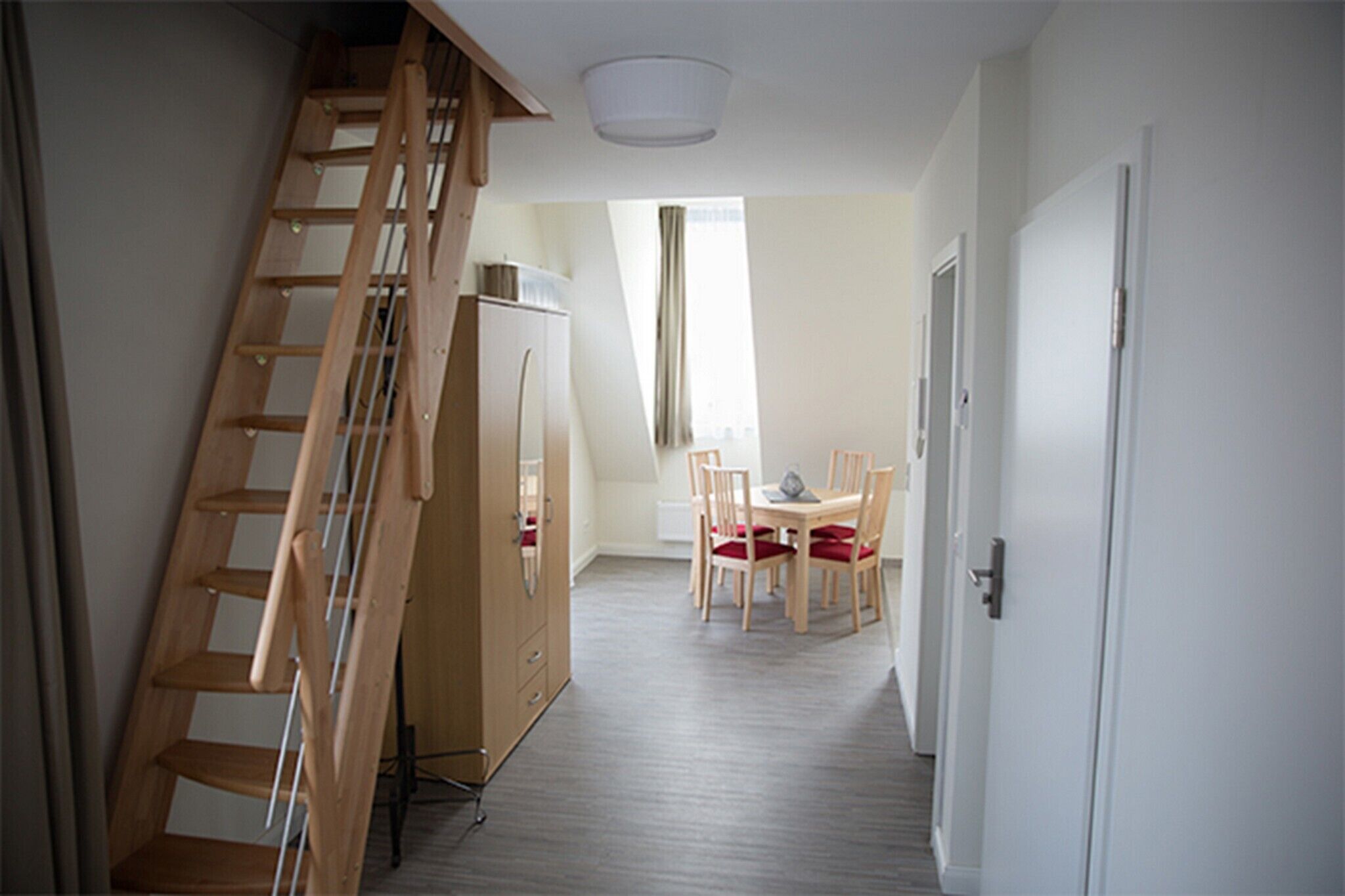 A hallway with a wooden staircase, a dining area with a table and chairs, and a refrigerator.