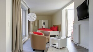 A modern hotel room with a large sliding glass door, a bed with red bedding, a white bedside table, a beige armchair, and a flat-screen TV mounted on the wall. - Domblick Schwerin (Schwerin)