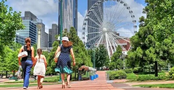 A park with a Ferris wheel, greenery, and modern buildings in the background.
