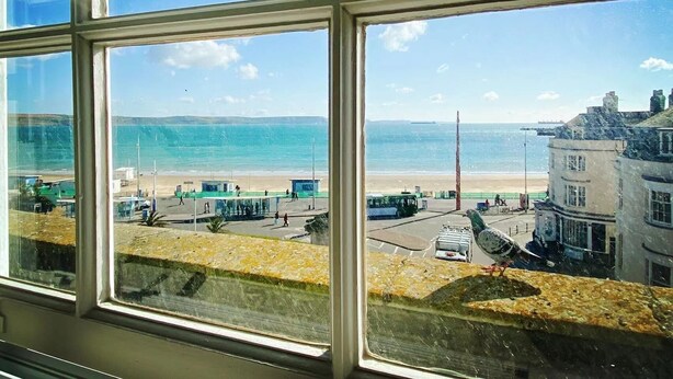 Vista a través de una ventana de una zona costera con playa, muelle y edificios.