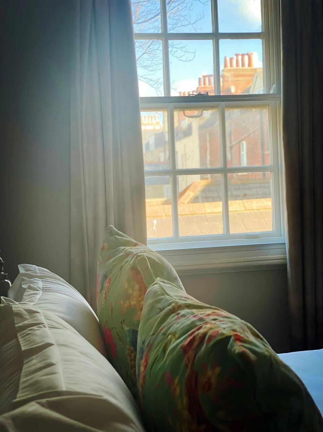 Un lit avec un coussin à motifs floraux et une vue sur des immeubles par la fenêtre.