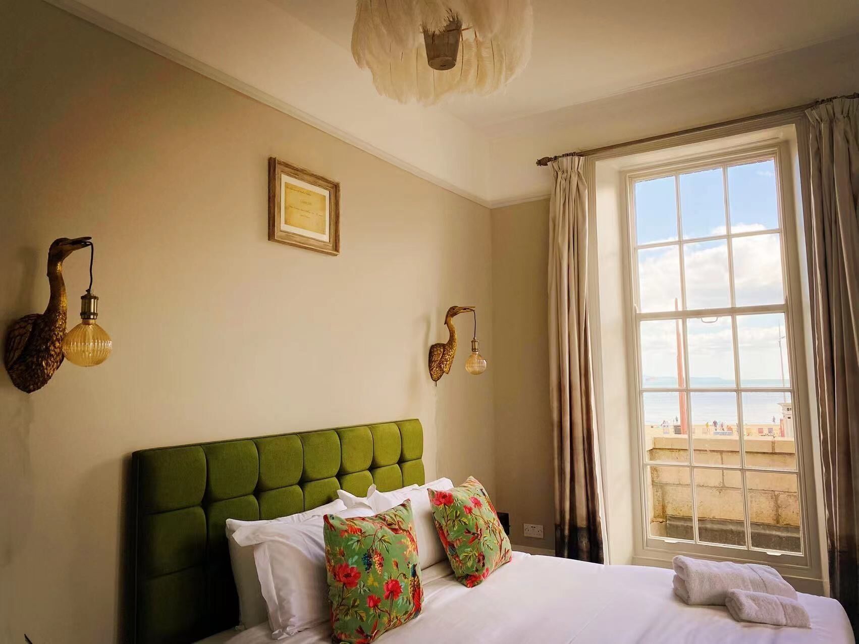 Ein Hotelzimmer mit einem grünen, gepolsterten Kopfteil, einem großen Fenster mit Vorhängen und Wandleuchten.