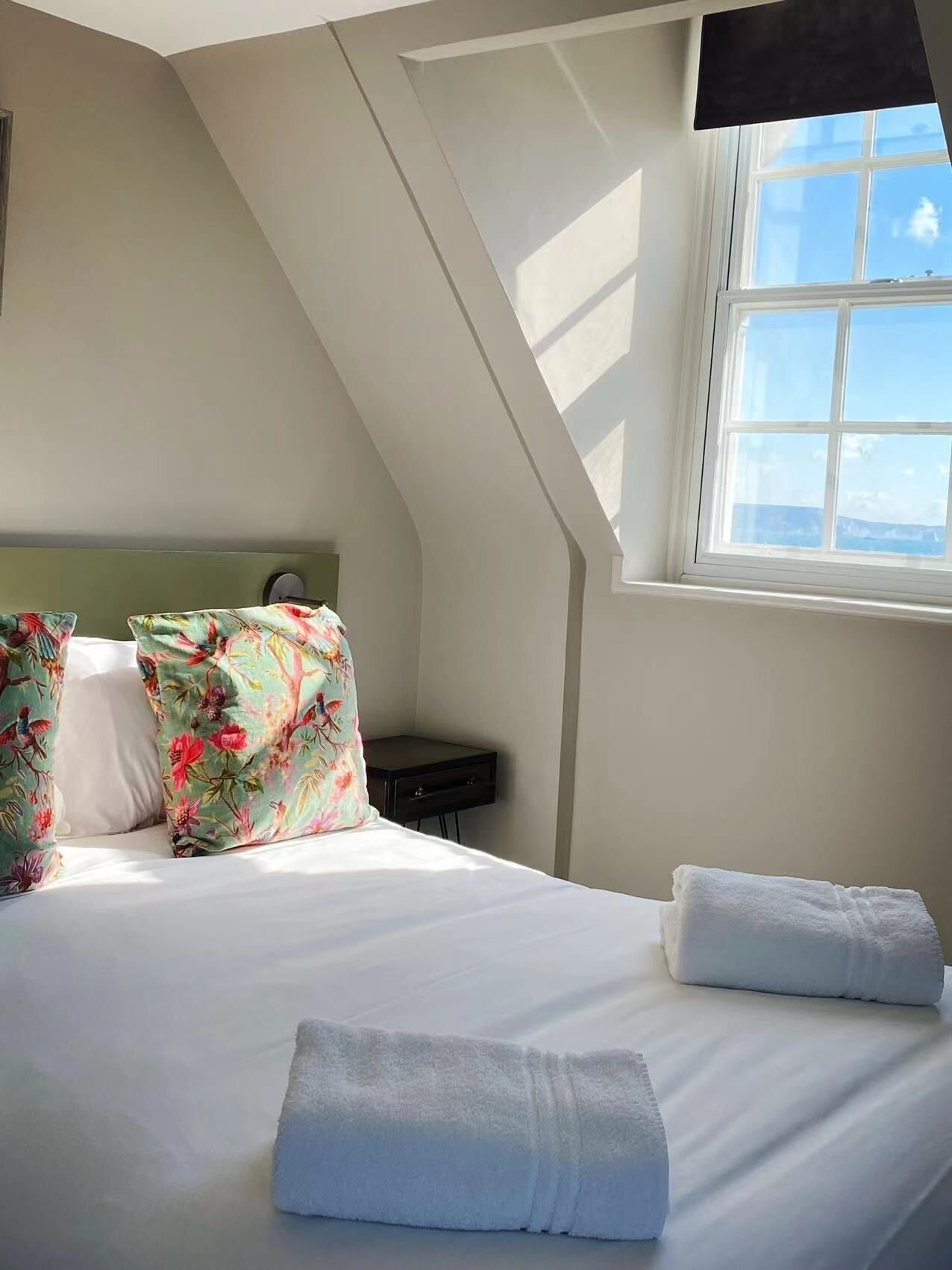 A bedroom with a bed, pillows, a nightstand, and a window.