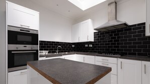 A modern kitchen with white cabinets, black tiled backsplash, stainless steel appliances, and a central island. - Hotel Orlando by PLI (London)