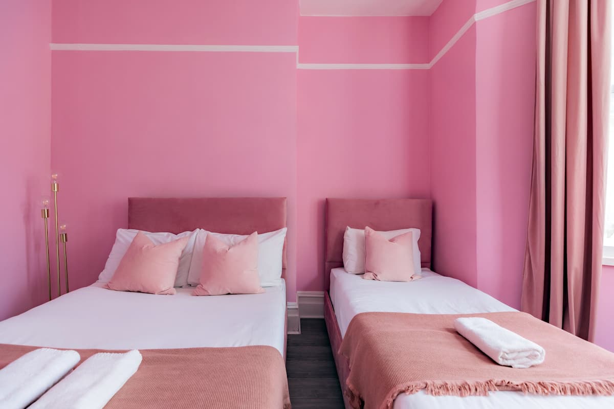A pink-themed hotel room with two beds, white bedding, and pink curtains.