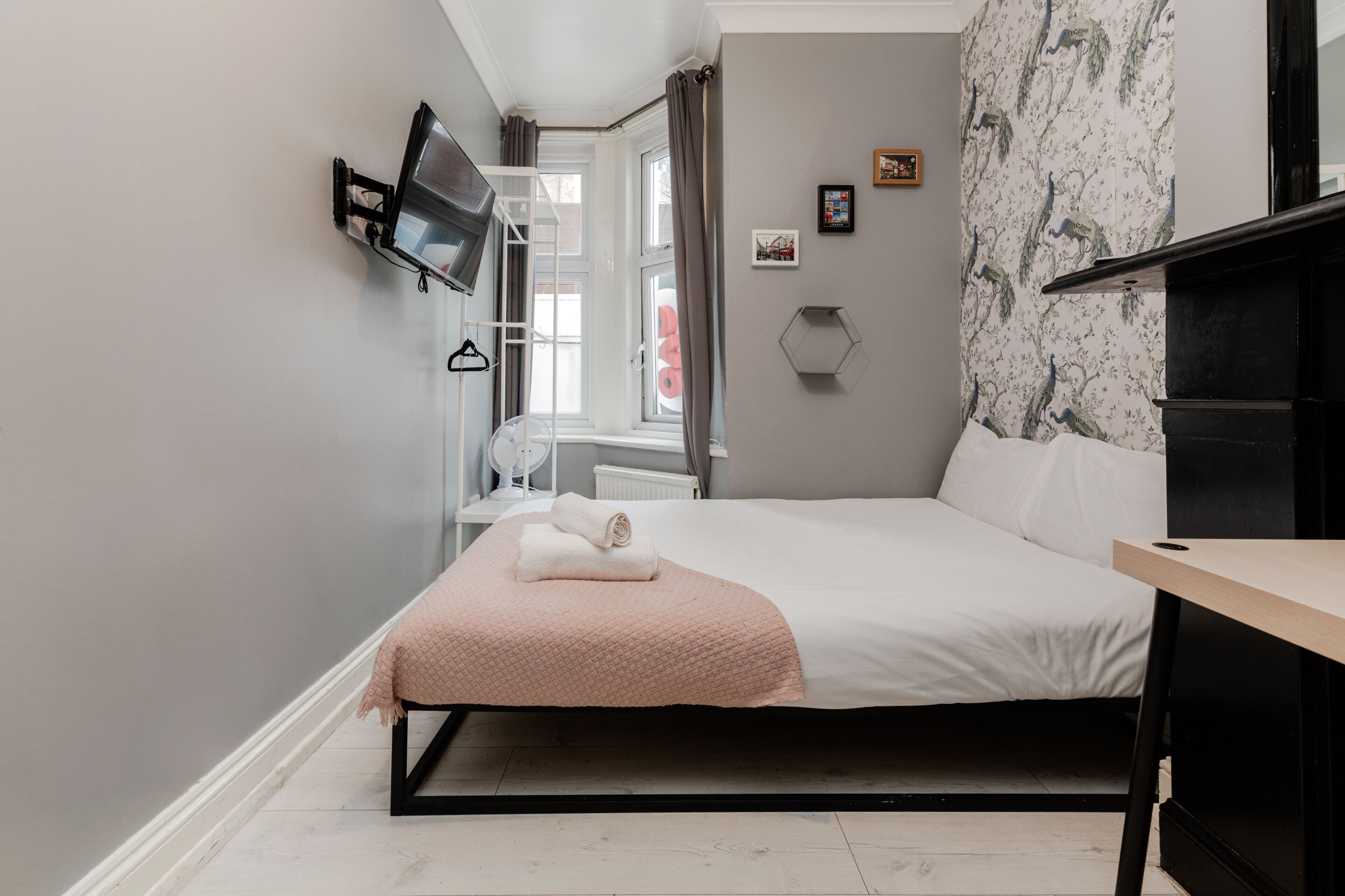 Ein modernes Schlafzimmer mit einem Bett, einem Schreibtisch, einem Fernseher und einem Fenster mit Vorhängen.