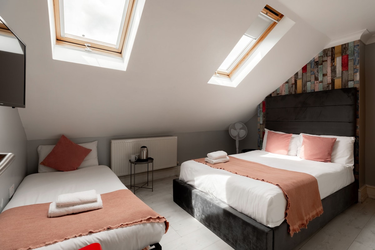 A modern bedroom with two beds, skylights, a radiator, and a fan.