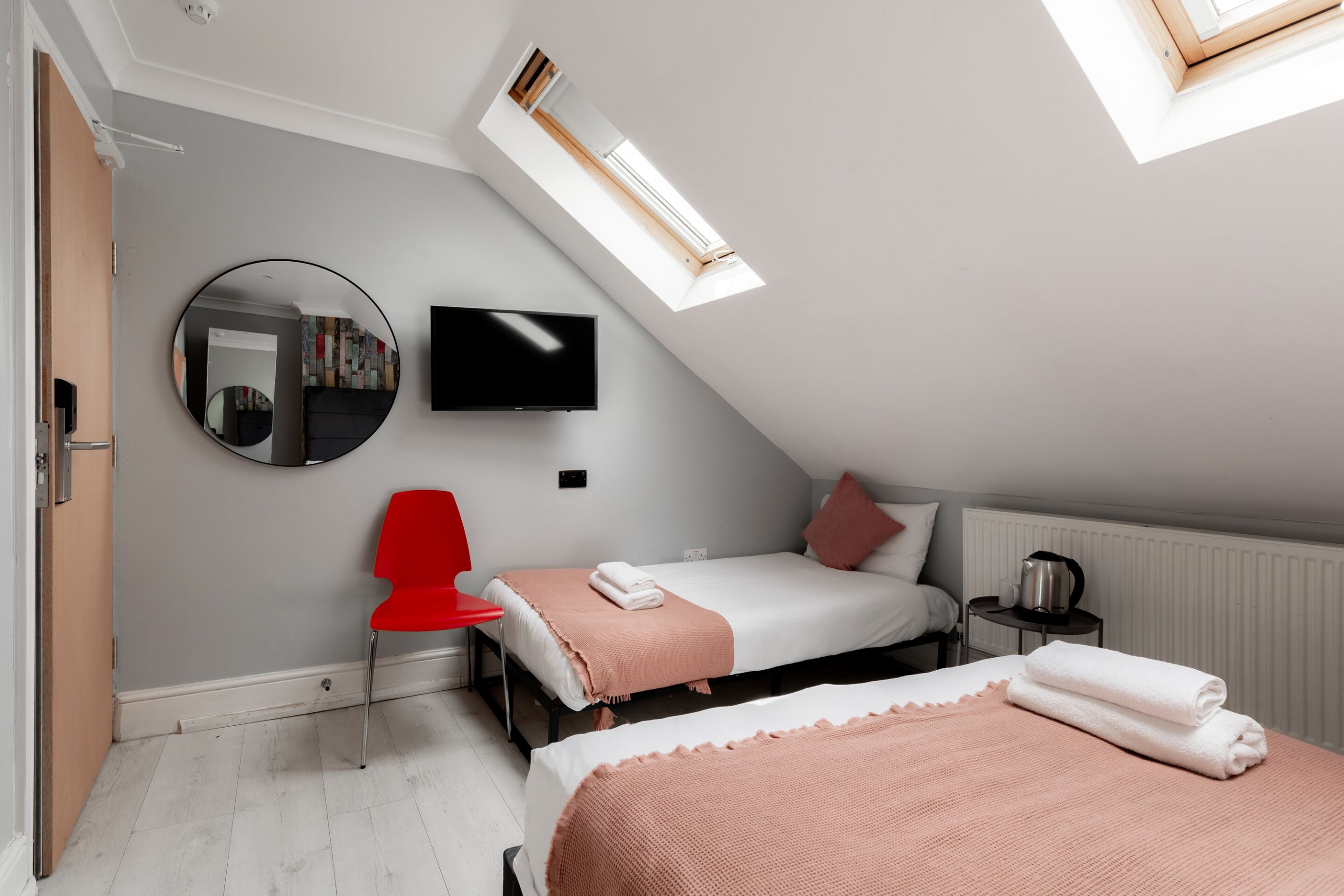 A modern bedroom with two beds, a red chair, a TV, and a skylight.