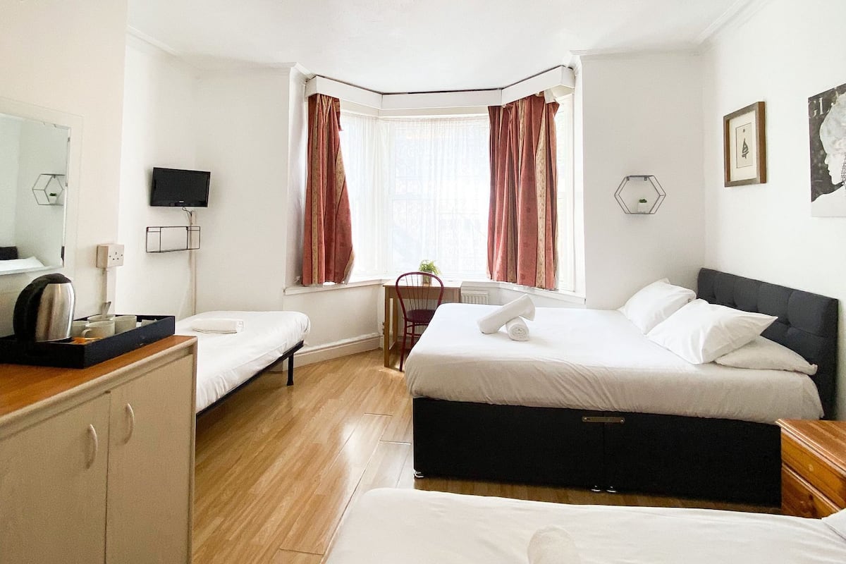 A hotel room with two beds, a desk, a TV, and a window with curtains.