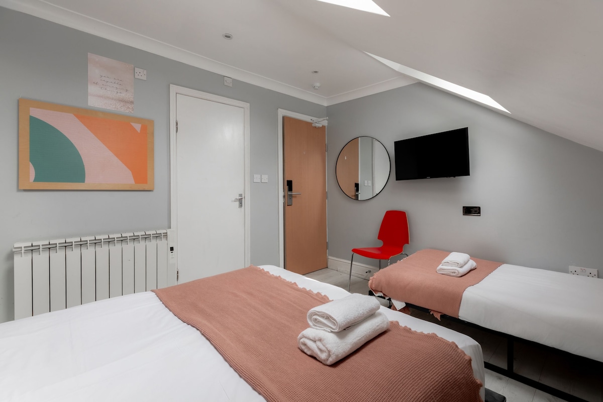 A hotel room with two beds, a red chair, a TV, and a painting on the wall.