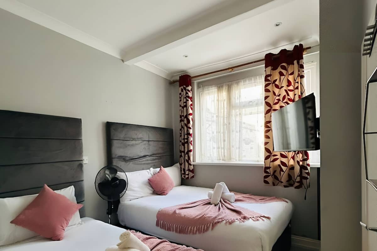 A hotel room with two beds, a ceiling fan, a TV, and a window with curtains.