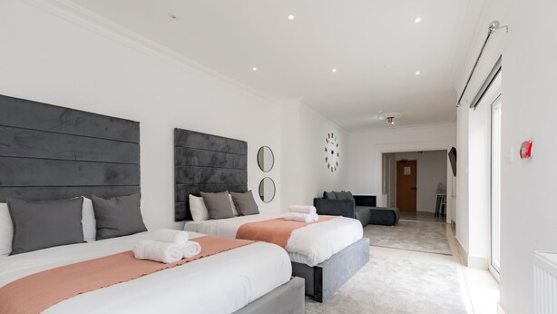 A modern hotel room with two beds, a large mirror, a clock, and a view of the hallway. - Hotel Orlando by PLI (London)