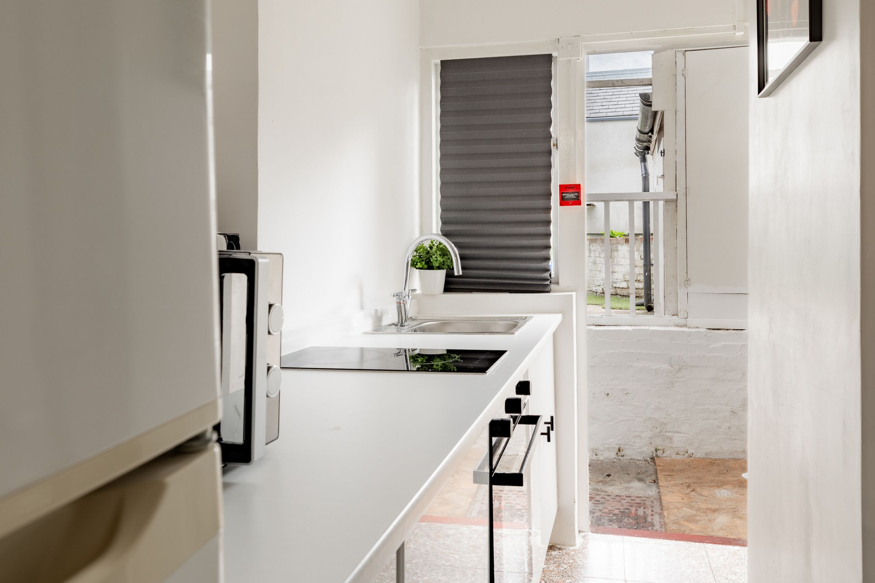 A modern kitchen with a white countertop, a sink, and a small potted plant.