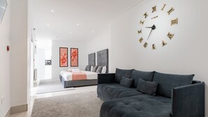 A modern bedroom with a large bed, a grey sofa, and a wall clock. - Hotel Orlando by PLI (London)