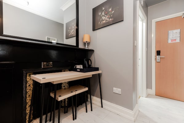 A compact room with a desk, chair, and a mirror. There is a door with a sign on it. - Hotel Orlando by PLI (London)