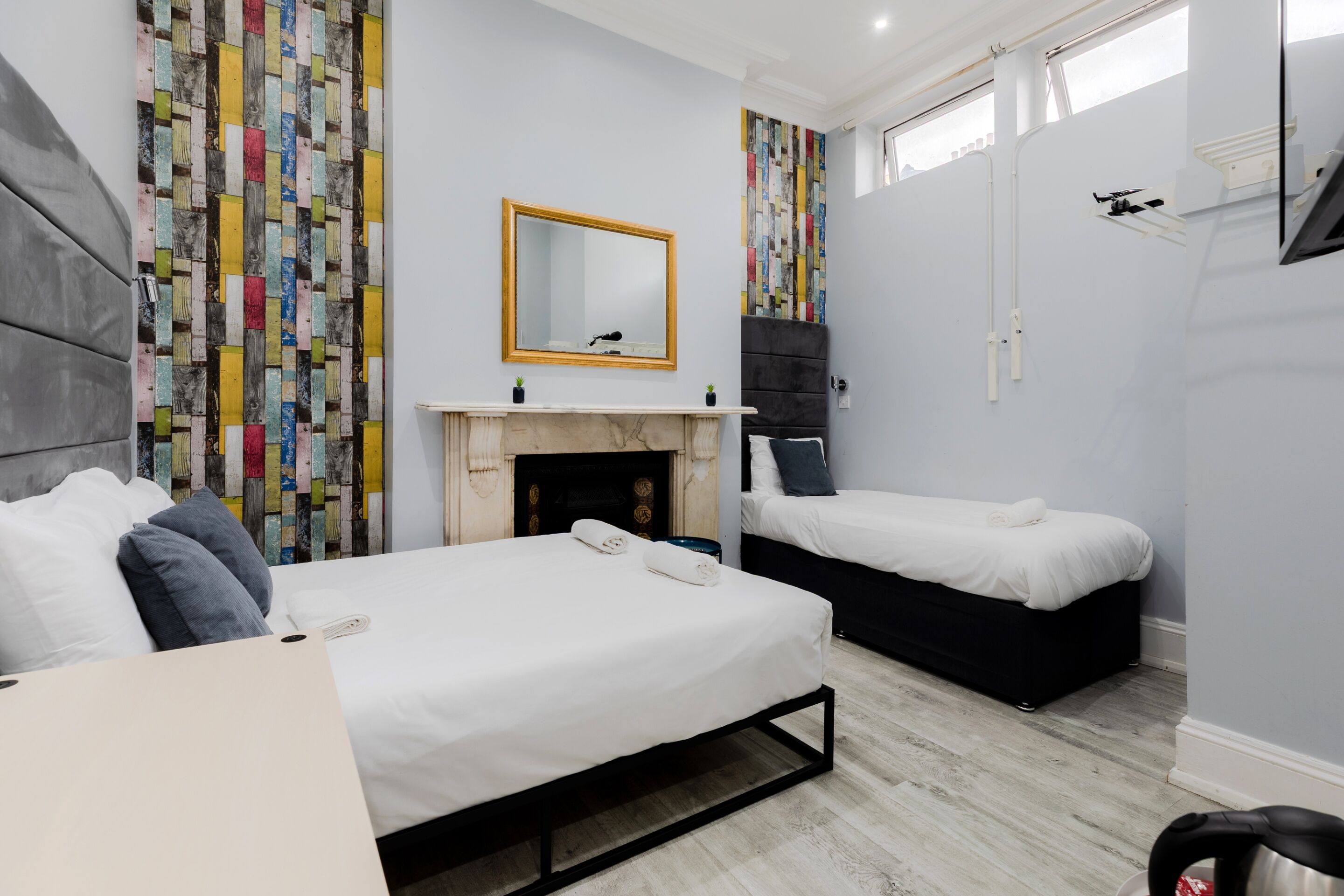 A modern bedroom with two beds, a fireplace, and a large mirror.
