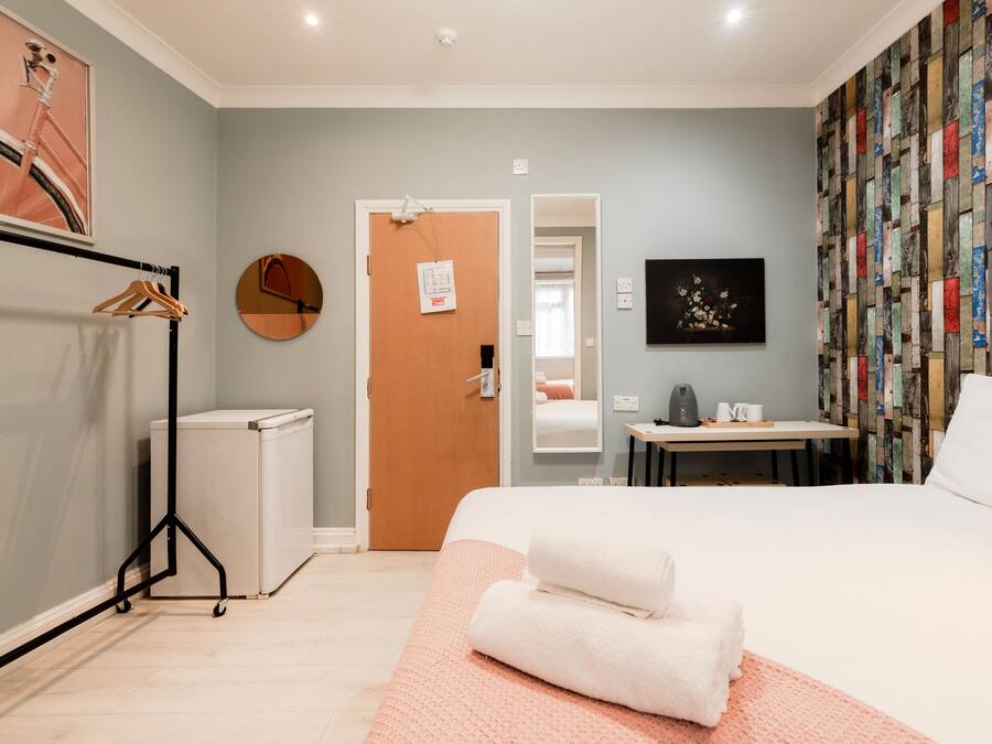 A hotel room with a bed, a desk, a chair, a wardrobe, and a mirror.