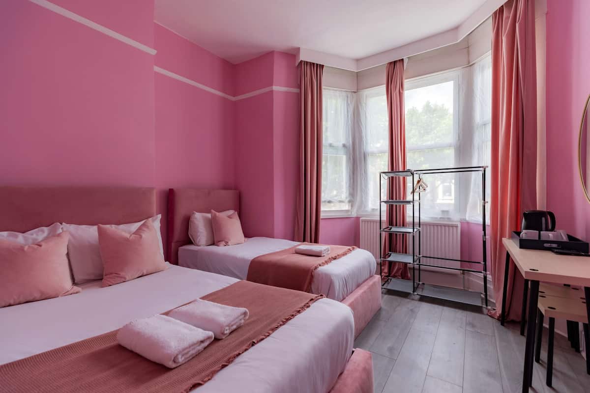 A pink-themed hotel room with two beds, a desk, and a radiator.