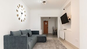 A modern living room with a grey sectional sofa, a wall clock, and a mounted TV. - Hotel Orlando by PLI (London)
