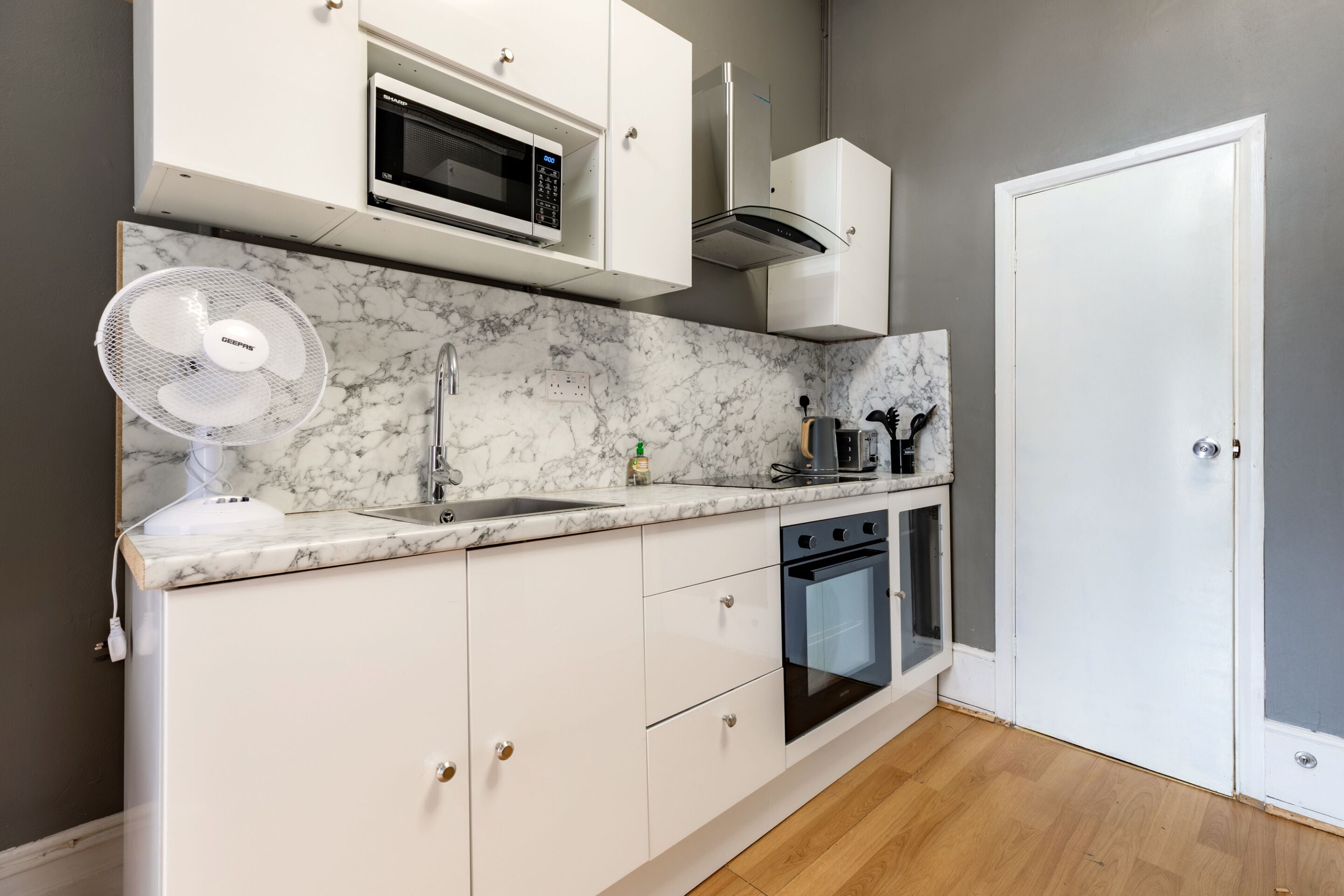 A modern kitchen with white cabinets, a built-in microwave, a fan, a sink, and an oven.
