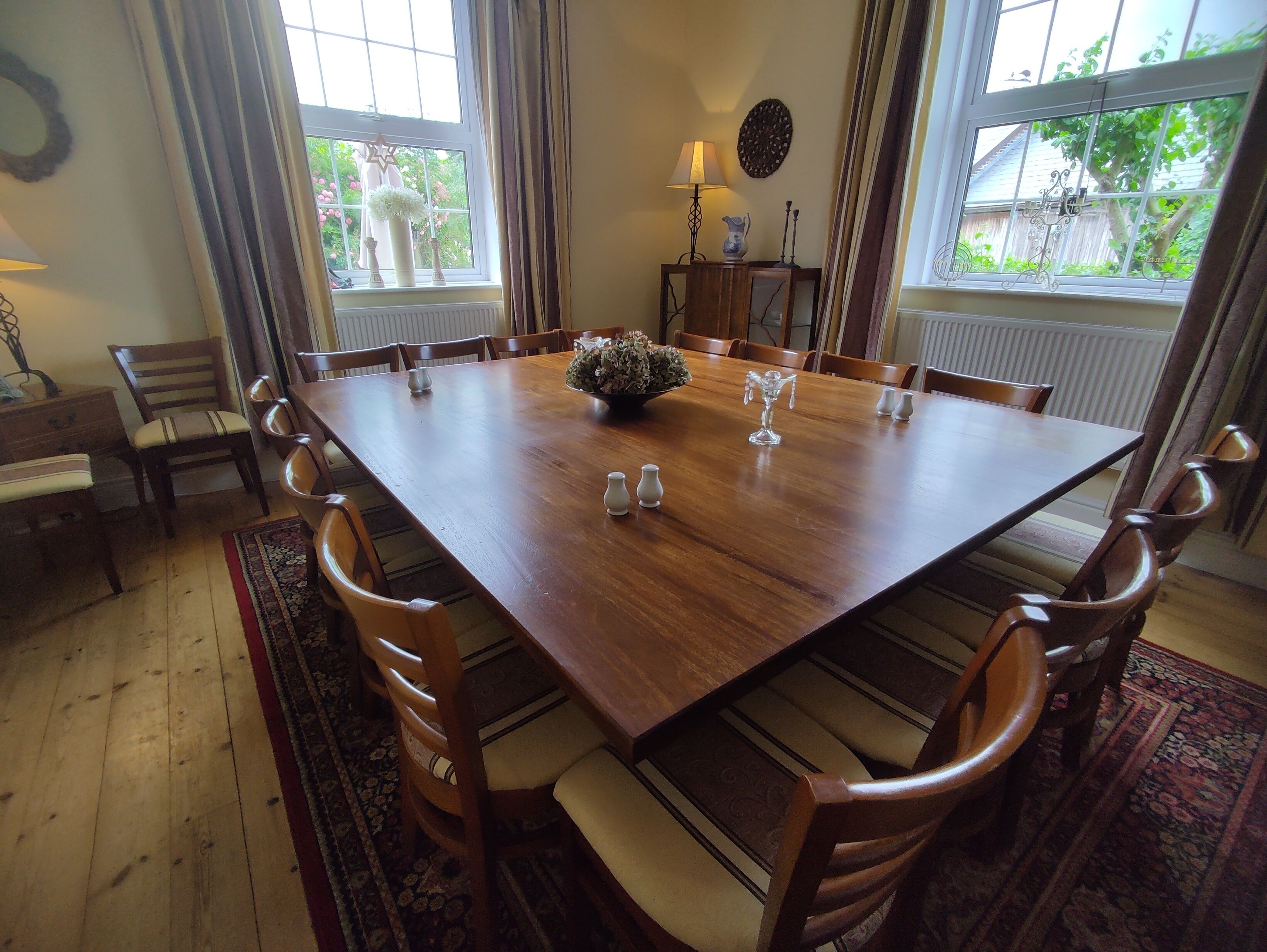 Ein Esszimmer mit einem großen Holztisch, mehreren Stühlen, einer Vase und einem kleinen Tisch mit einer Lampe.
