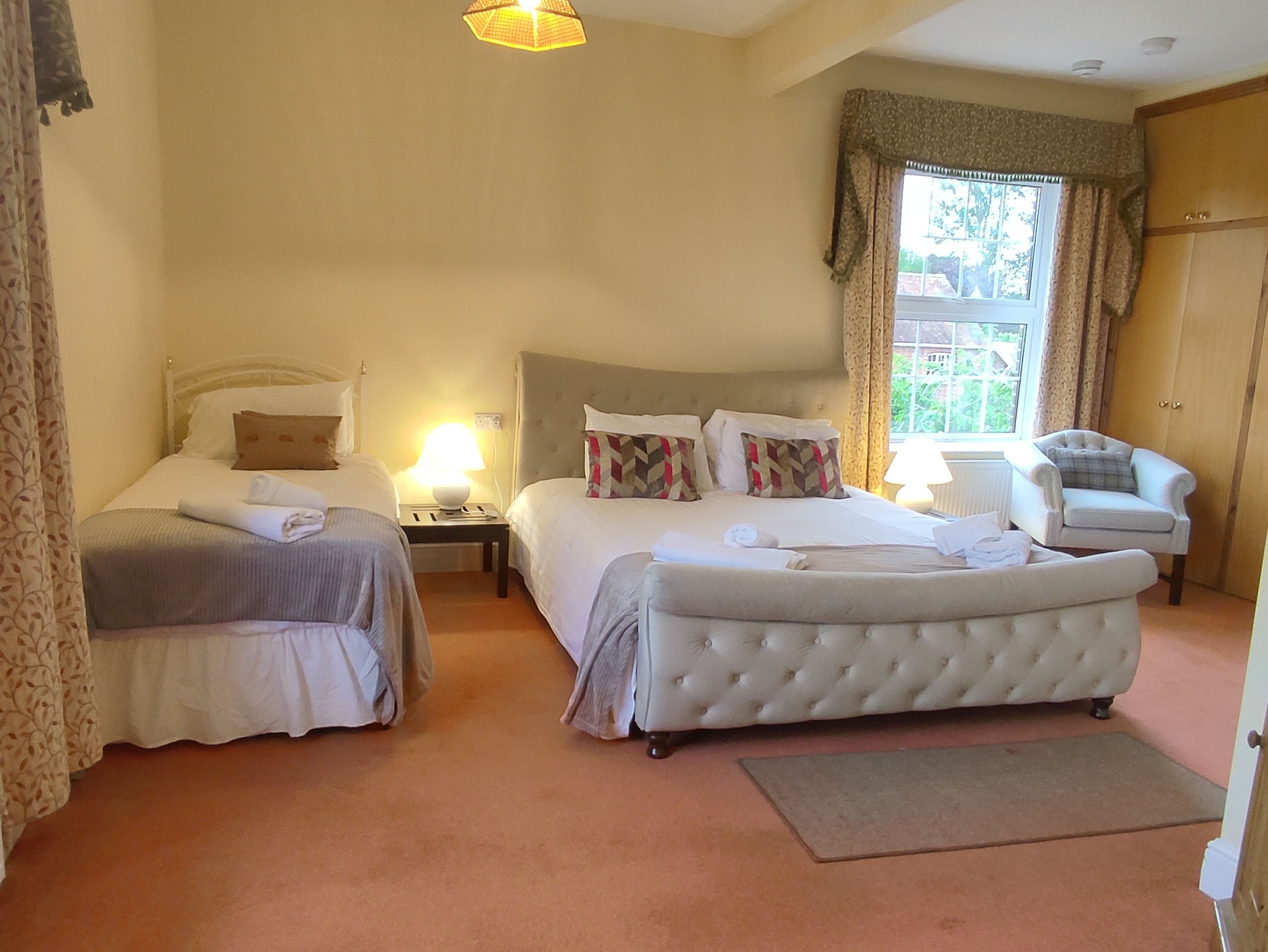A hotel room with two beds, a sitting area with a chair, and a view of the outdoors through a window.