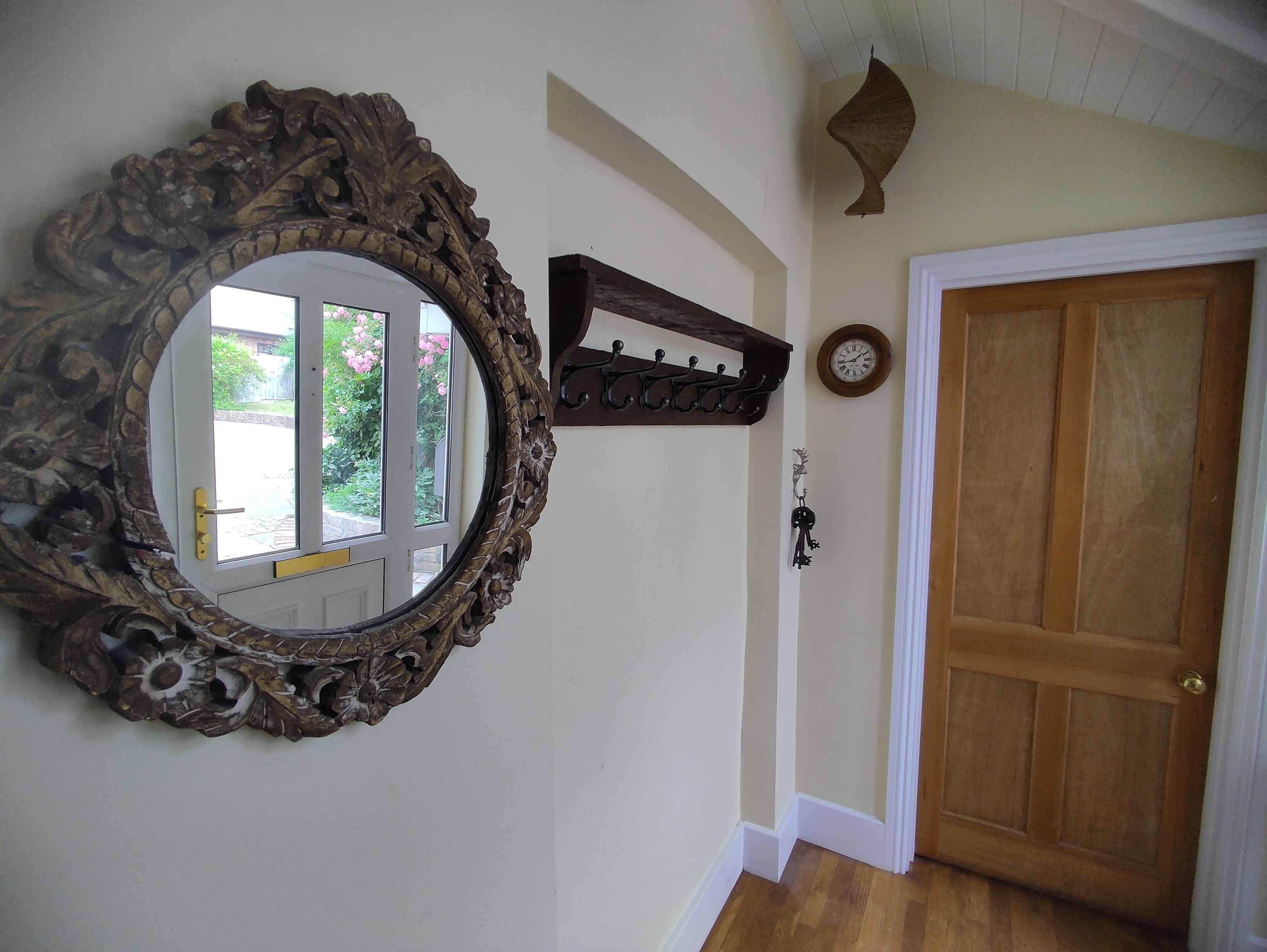 Un corridoio con una porta in legno, una sveglia a parete e uno specchio decorato con motivi floreali.