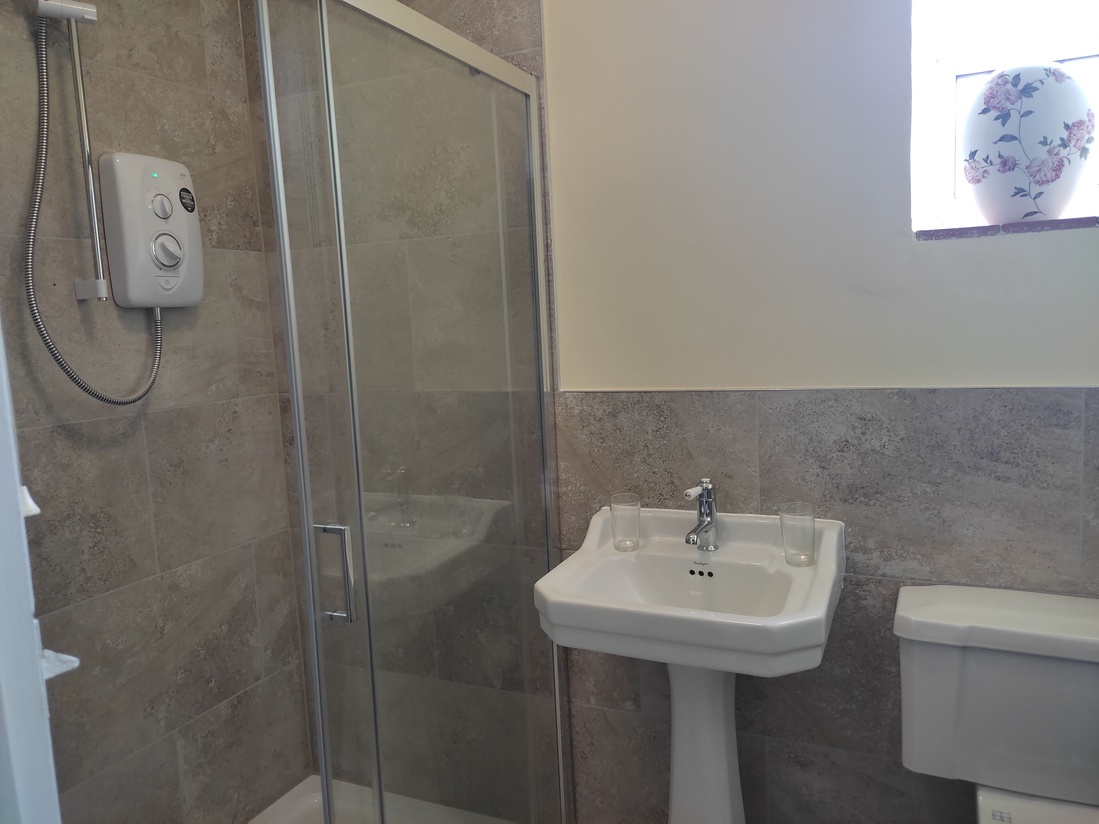 Un bagno con doccia vetrata, lavabo su piedistallo e water.