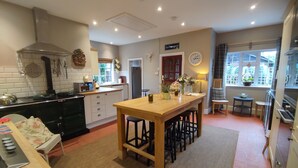 A kitchen with a central island, wooden stools, a clock, and a window with a view. - The Cheese House (Salisbury)