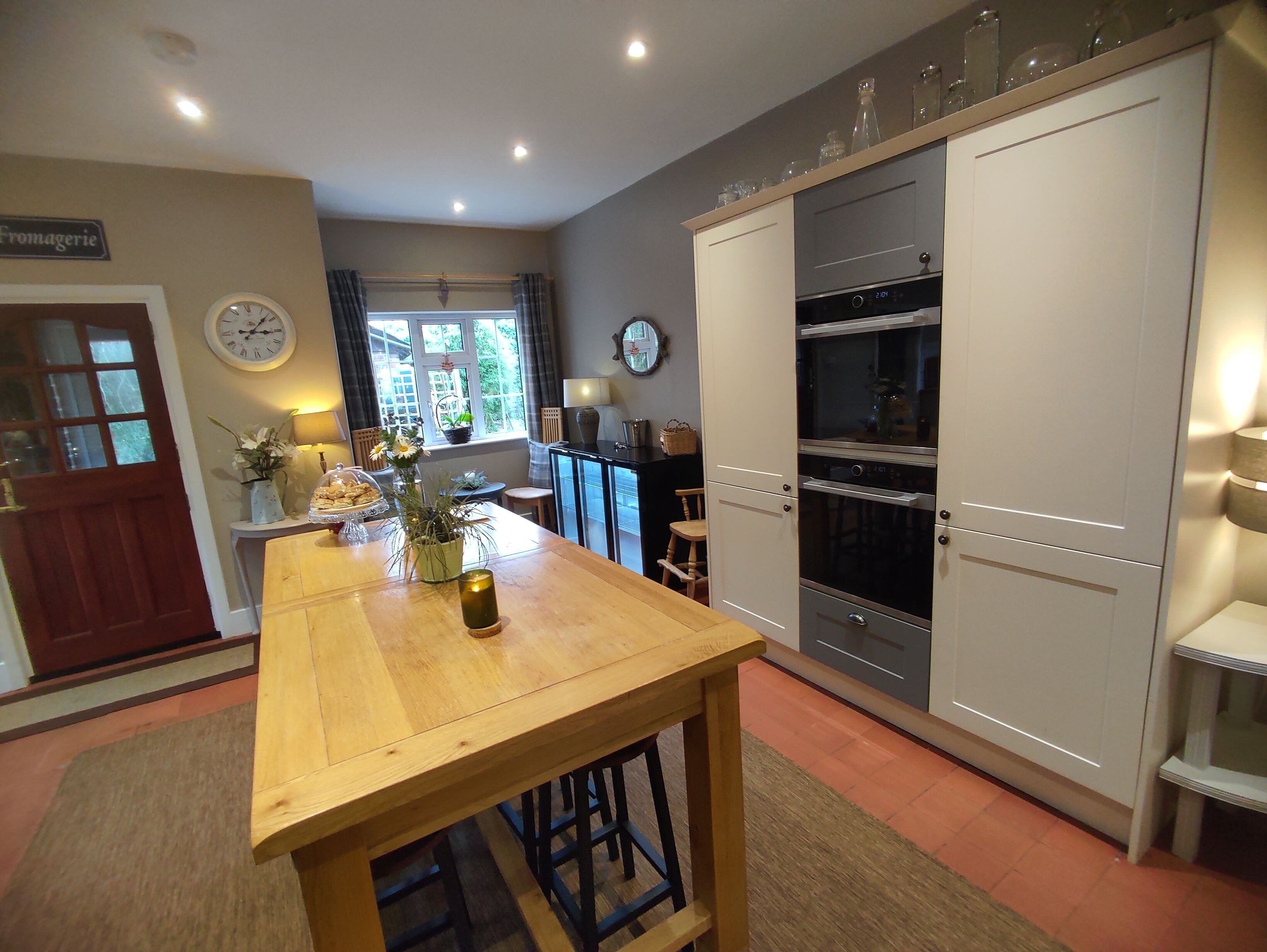 A kitchen with a wooden table, a clock, and a window with curtains.