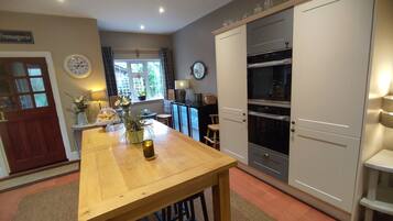 A kitchen with a wooden table, a clock, and a window with curtains.