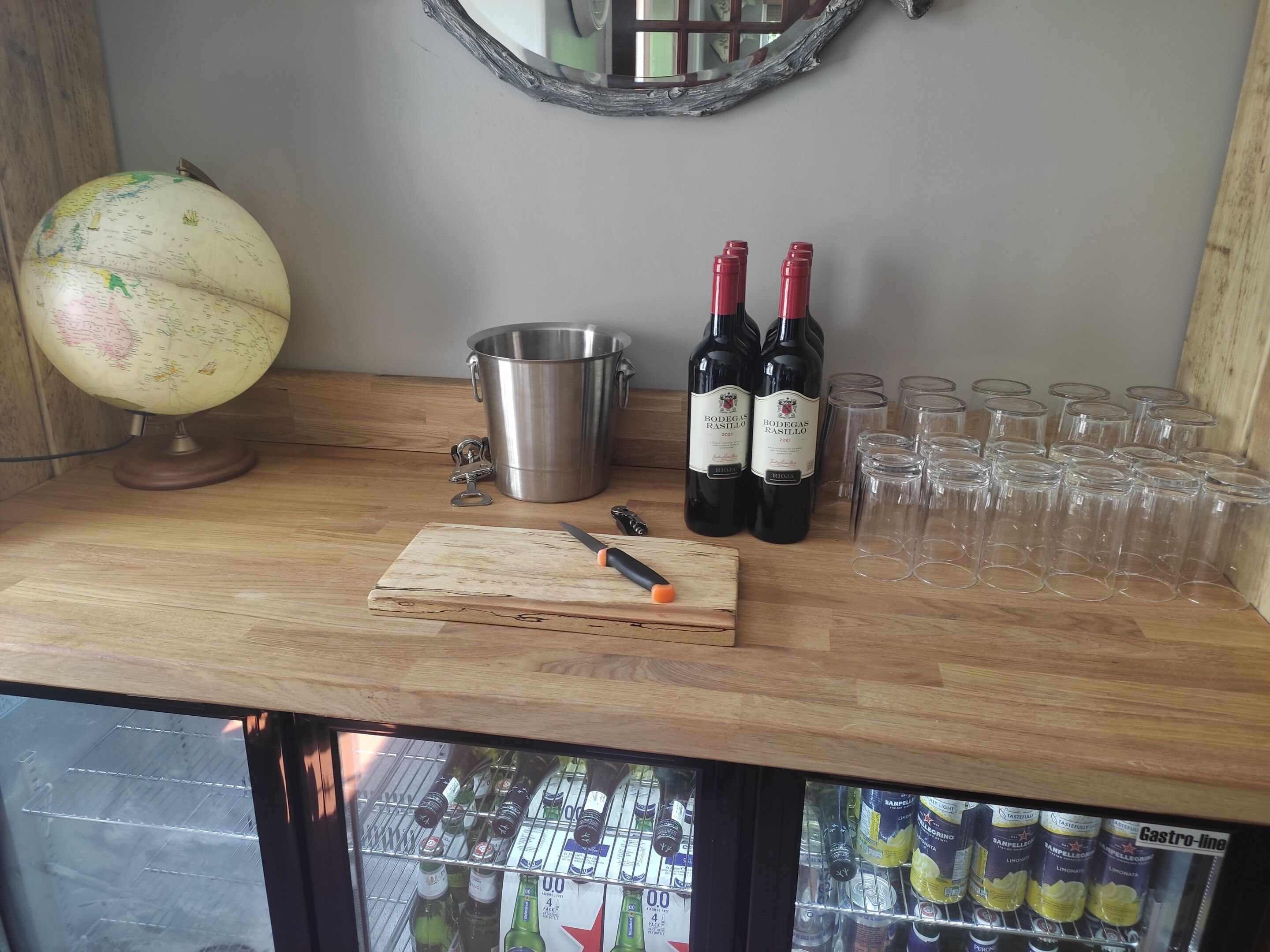 A wooden bar counter with a globe, wine bottles, glasses, and a cutting board.