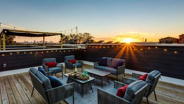 A rooftop patio with outdoor furniture, string lights, and a sunset view.